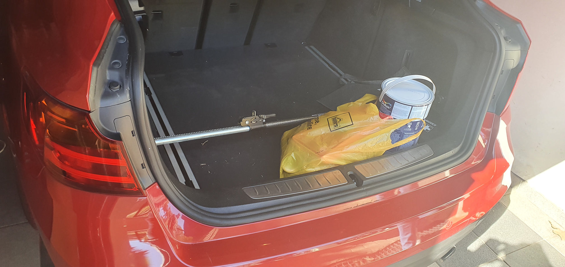 Ratchet-type cargo bar installed in car boot holding paint bucket and other diy supplies in place.