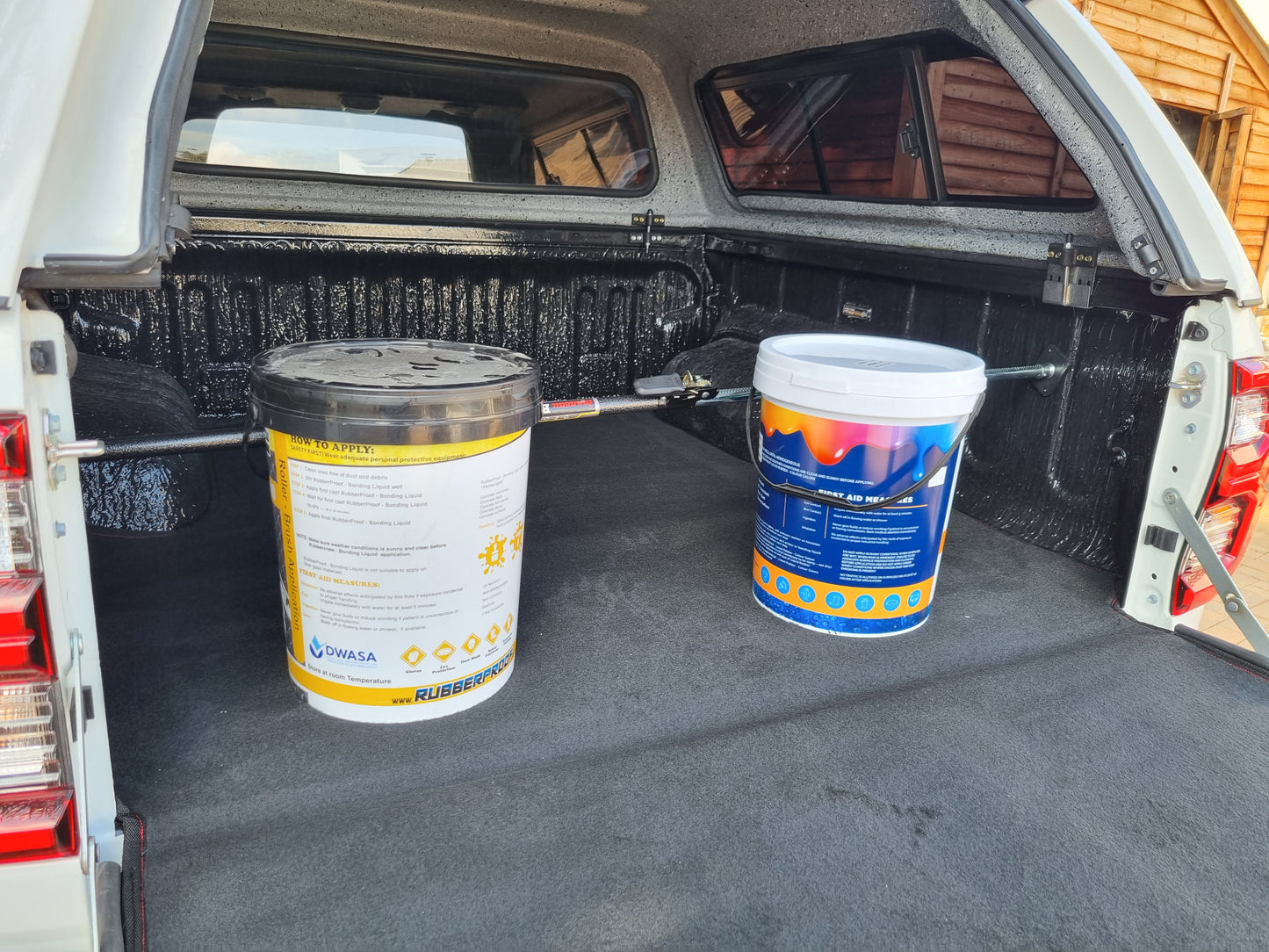 Ratchet-type cargo bar installed on back of utility vehicle with canopy holding two paint buckets in place.