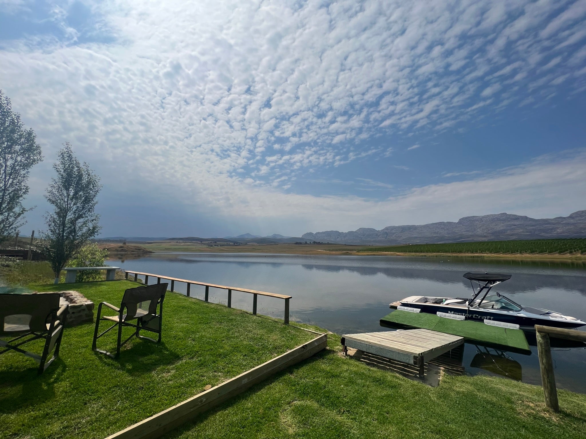 Tranquil lake with power boat and camp chairs on grass in foreground.