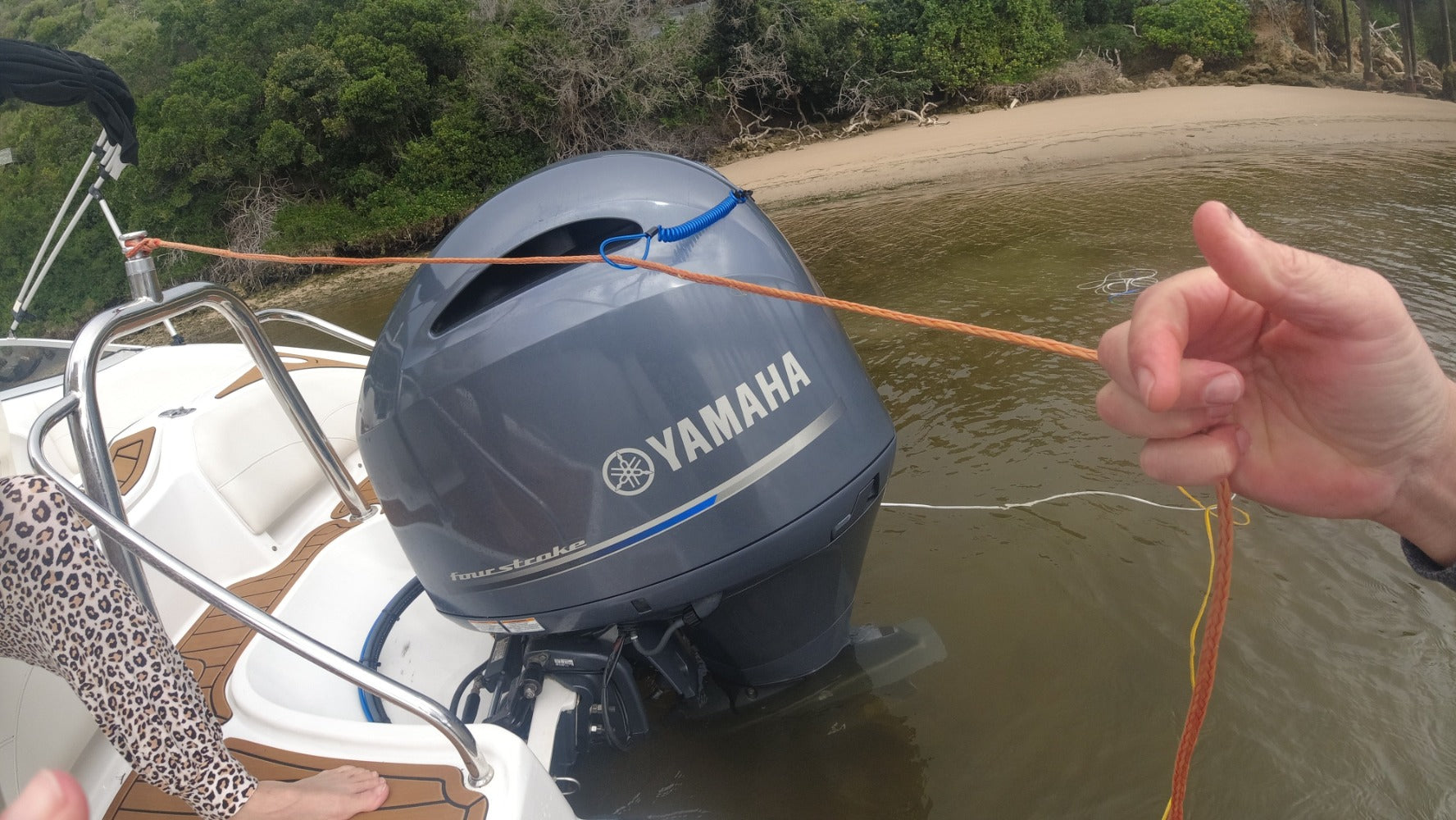 Mala hand holding ski rope in front of power boat engine on lake.