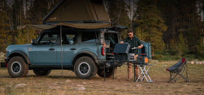 Jackery Explorer 1000 portable power station used outdoors during camping next to off-road SUV.