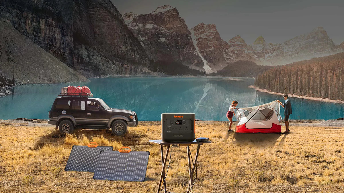 Couple setting up camp near scenic lake with portable power station and solar panels set up next to off-road vehicle.